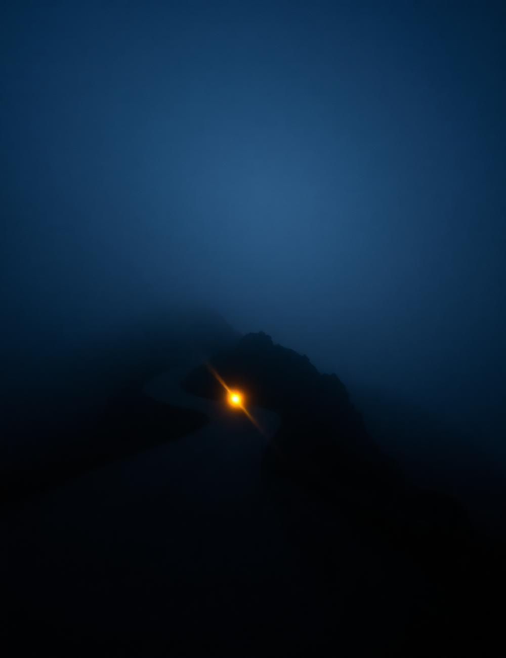 Foggy mountain road at dawn with a single headlight