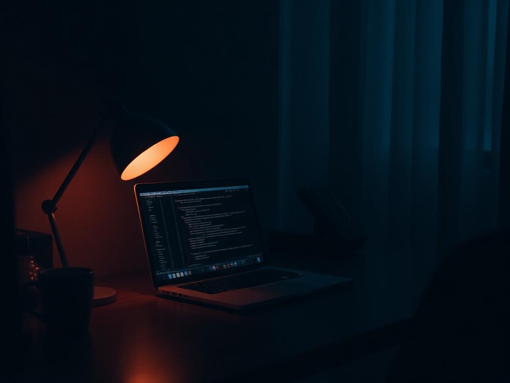 Laptop glowing in a dim room beside a warm lamp